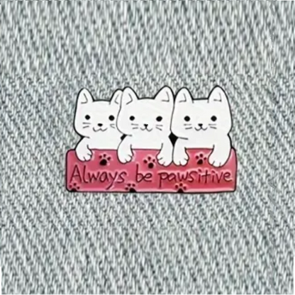 enamel pin with 3 cute white cats saying always be pawsitive, over a jeans fabric