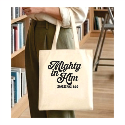 Tote bag with 'Mighty in Him Ephesians 6:10' text held by a person in a library setting.