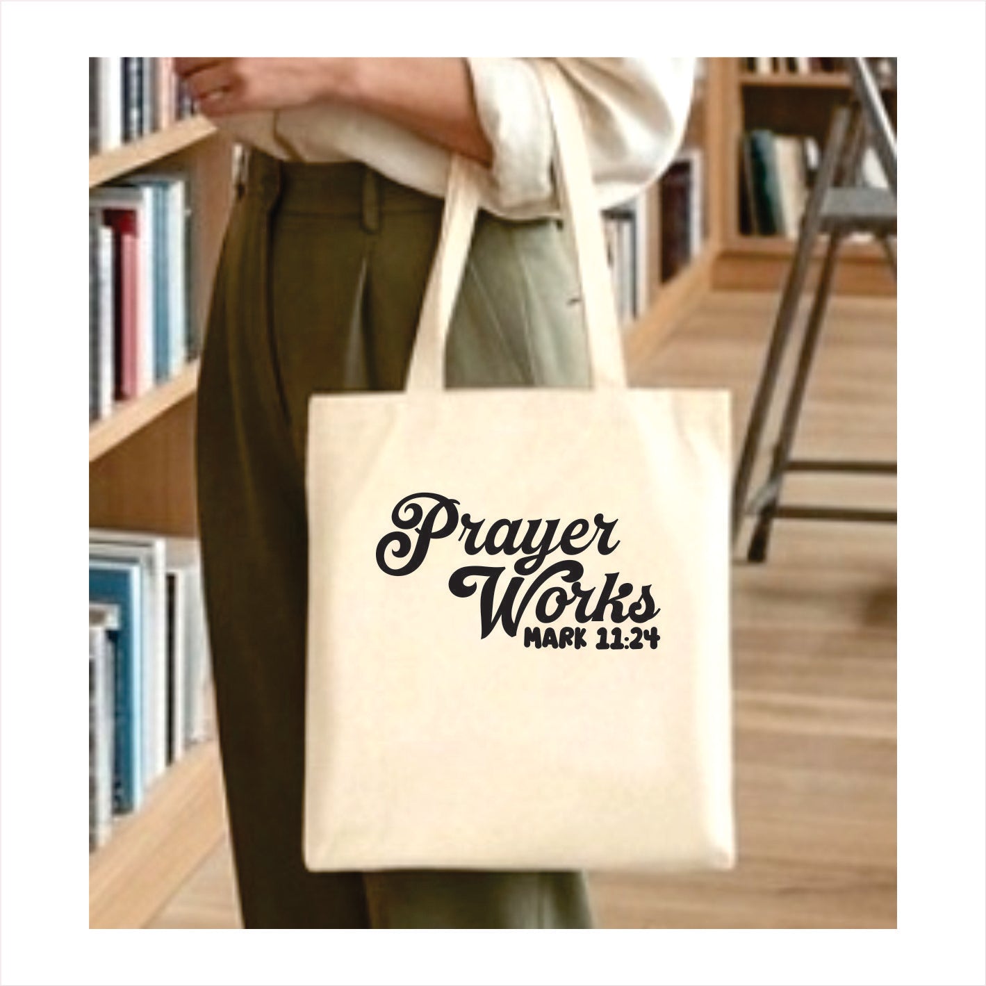 Tote bag with 'Prayer Works' text held by a person in a library setting