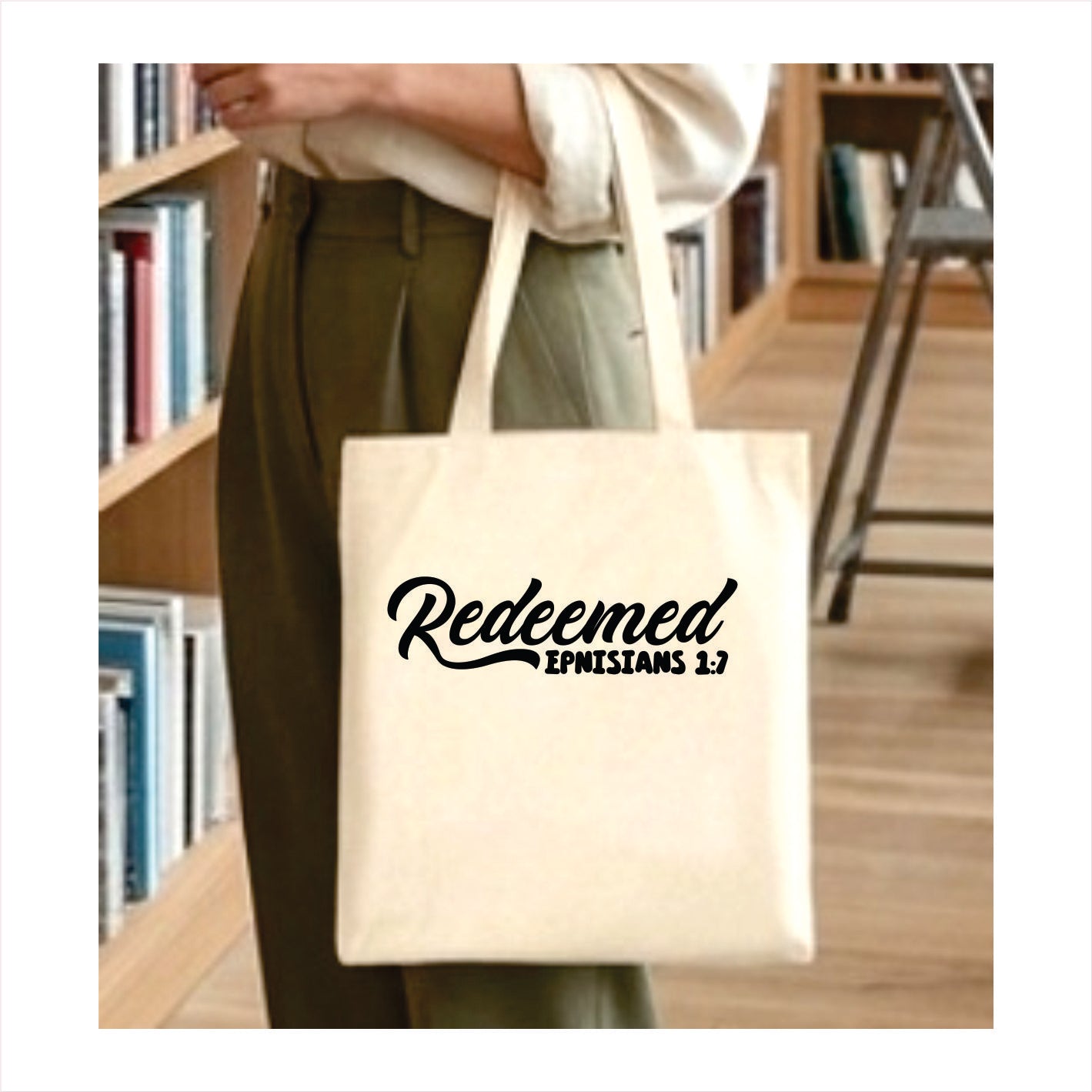 Person holding a tote bag with 'Redeemed Ephesians 1:7' text in a library setting.