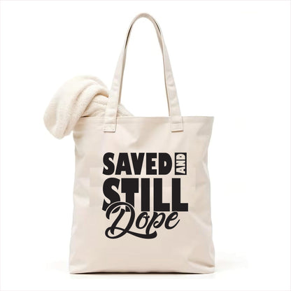 white tote bag with 'Saved and Still Dope' text on a white background