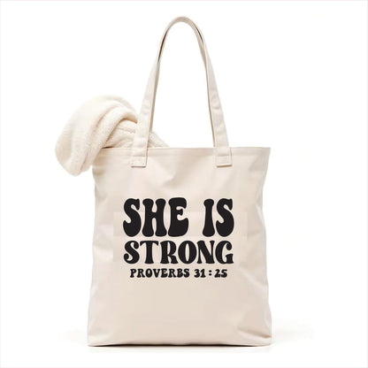 white tote bag with 'SHE IS STRONG Proverbs 31:25' text on a white background